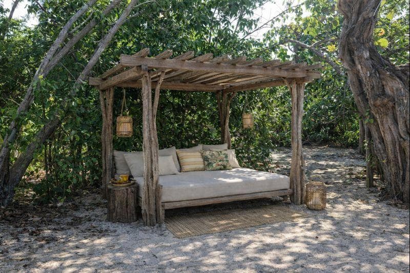 Rustic daybed under a natural pergola surrounded by tropical greenery